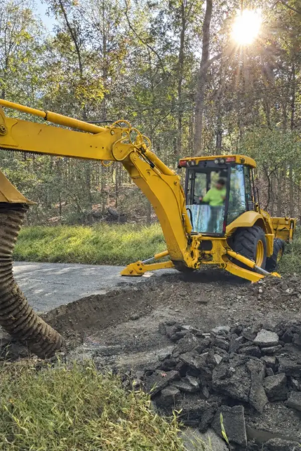 Backhoe excavating for drainage work beside a paved drive