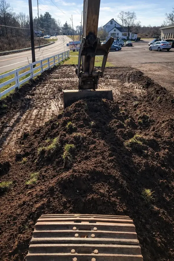 Excavator reshaping a site beside an existing roadway