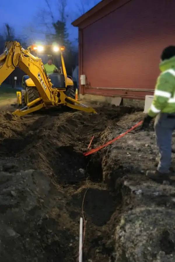Backhoe excavating a utility trench beside a building